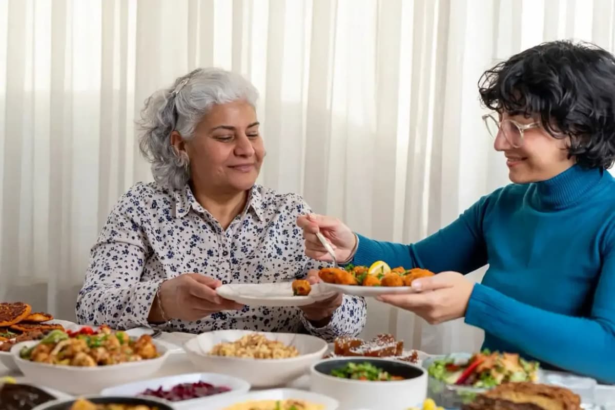 İki kişi, çeşitli yemeklerin bulunduğu sofrada tabaklarına yemek servis ediyor.
