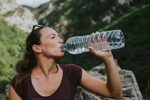 Doğada yürüyüş yaparken büyük, şeffaf bir plastik şişeden su içen bir kadın.